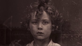 Movie still from “Days of Heaven” (1978), directed by Terrence Malick – A young boy with curly brown hair is looking at the camera; Extreme Close Up shot, Overhead angle