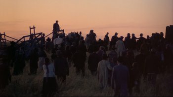 Movie still from “Days of Heaven” (1978), directed by Terrence Malick – A group of people standing on top of a grass covered field; Extreme Wide shot, Low angle