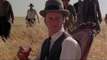 Movie still from “Days of Heaven” (1978), directed by Terrence Malick – A man in a hat holding a drink in a field; Close Up shot, Low angle