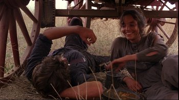 Movie still from “Days of Heaven” (1978), directed by Terrence Malick – A man and a woman sitting on the ground in a field; Medium shot, Low angle