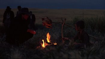 Movie still from “Days of Heaven” (1978), directed by Terrence Malick – A man and a woman sitting in front of an open fire in a field at night; Medium shot, Over the shoulder angle