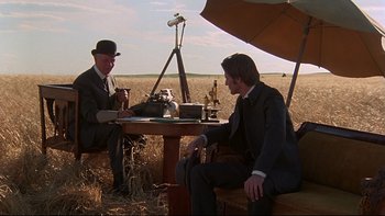 Movie still from “Days of Heaven” (1978), directed by Terrence Malick – Two men sitting at a table in the middle of a field; Wide shot, Over the shoulder angle