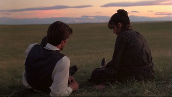 Movie still from “Days of Heaven” (1978), directed by Terrence Malick – A man and a woman sitting in the grass; Wide shot, Over the shoulder angle