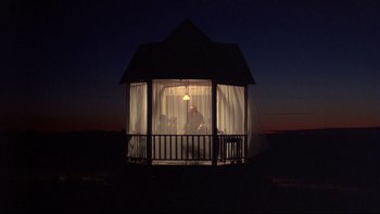 Movie still from “Days of Heaven” (1978), directed by Terrence Malick – A gazebo lit up at night with a person sitting in it; Extreme Wide shot, Low angle