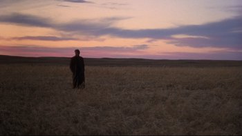 Movie still from “Days of Heaven” (1978), directed by Terrence Malick – A man standing in the middle of an open field at sunset; Extreme Wide shot, Over the shoulder angle