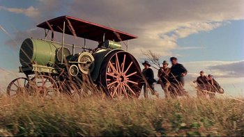 Movie still from “Days of Heaven” (1978), directed by Terrence Malick – Three men standing next to an old fashioned tractor; Wide shot, Low angle