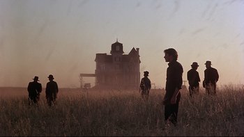 Movie still from “Days of Heaven” (1978), directed by Terrence Malick – A group of people standing in a field near a house; Wide shot, Low angle