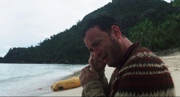 Movie still from “Cast Away” (2000), directed by Robert Zemeckis – A man with wet hair and a wet sweater on , holding his hands to his face , near the ocean; Medium shot, High angle