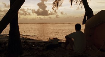 Movie still from “Cast Away” (2000), directed by Robert Zemeckis – A man sitting on the beach looking out at the ocean; Extreme Wide shot, High angle