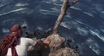 Movie still from “Cast Away” (2000), directed by Robert Zemeckis – A person reaching for a tree on a cliff by the ocean; Extreme Wide shot, Overhead angle