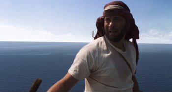 Movie still from “Cast Away” (2000), directed by Robert Zemeckis – A man wearing a head scarf standing on top of a hill; Medium shot, Low angle