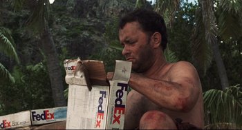 Movie still from “Cast Away” (2000), directed by Robert Zemeckis – A shirtless man holding a fedex box in his hands; Medium shot, Low angle