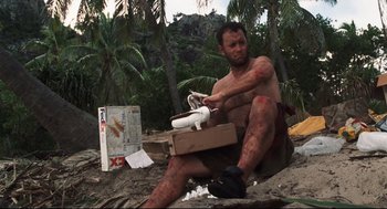 Movie still from “Cast Away” (2000), directed by Robert Zemeckis – A man sitting on the ground holding a nintendo wii game controller; Wide shot, Low angle