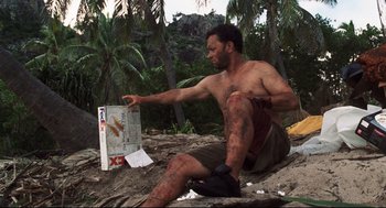 Movie still from “Cast Away” (2000), directed by Robert Zemeckis – A man sitting on the ground next to a box of cigarettes; Medium shot, Low angle