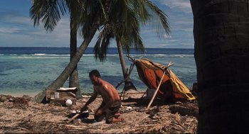 Movie still from “Cast Away” (2000), directed by Robert Zemeckis – A man sitting on the ground near a tent on the beach; Wide shot, High angle