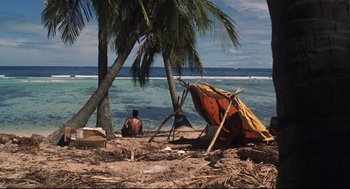 Movie still from “Cast Away” (2000), directed by Robert Zemeckis – A man sitting on the beach next to an umbrella; Extreme Wide shot, High angle