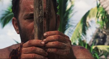 Movie still from “Cast Away” (2000), directed by Robert Zemeckis – A man with his hands on a stick in front of a tree; Close Up shot, Low angle