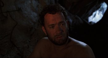 Movie still from “Cast Away” (2000), directed by Robert Zemeckis – A man with a beard is sitting in a cave; Close Up shot, High angle
