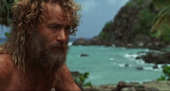 Movie still from “Cast Away” (2000), directed by Robert Zemeckis – A man with a long beard is sitting on a rock by the ocean; Close Up shot, Low angle