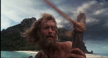 Movie still from “Cast Away” (2000), directed by Robert Zemeckis – A man with long hair and a long beard holding a stick; Medium shot, Low angle