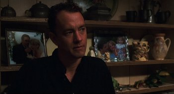 Movie still from “Cast Away” (2000), directed by Robert Zemeckis – A man in a black shirt in a room with pictures; Close Up shot, Over the shoulder angle