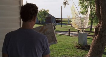 Movie still from “Cast Away” (2000), directed by Robert Zemeckis – A man standing in the grass holding a newspaper; Medium shot, Over the shoulder angle
