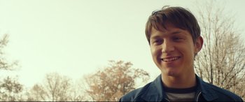 Movie still from “Cherry” (2021), directed by Joe Russo – A young man smiling for the camera with trees in the background; Close Up shot, Over the shoulder angle