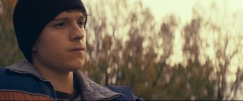 Movie still from “Cherry” (2021), directed by Joe Russo – A young man is looking into the distance with trees in the background; Close Up shot, Low angle