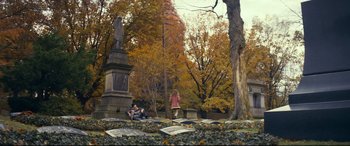 Movie still from “Cherry” (2021), directed by Joe Russo – A group of people sitting on a bench in a cemetery; Extreme Wide shot, High angle