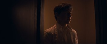 Movie still from “Cherry” (2021), directed by Joe Russo – A young man is looking into a mirror in the dark; Medium shot, Over the shoulder angle