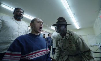 Movie still from “Cherry” (2021), directed by Joe Russo – A man and a man in a uniform talking to each other in front of a group of people; Medium shot, Low angle