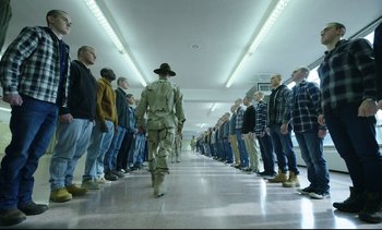 Movie still from “Cherry” (2021), directed by Joe Russo – A group of men standing in a line in a hallway; Wide shot, High angle