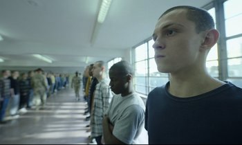 Movie still from “Cherry” (2021), directed by Joe Russo – A group of men standing in a line in front of a window; Medium shot, Low angle