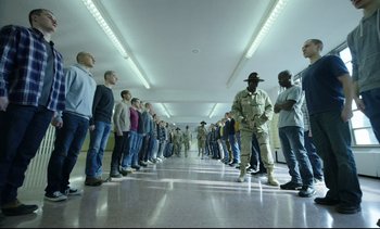 Movie still from “Cherry” (2021), directed by Joe Russo – A group of men standing in a line in a building; Wide shot, High angle
