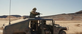 Movie still from “Cherry” (2021), directed by Joe Russo – A man with a gun on top of a vehicle; Wide shot, High angle
