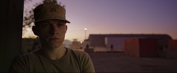 Movie still from “Cherry” (2021), directed by Joe Russo – A man wearing a hat in a parking lot at dusk; Close Up shot, Over the shoulder angle
