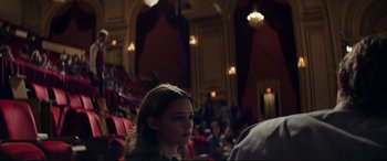 Movie still from “Cherry” (2021), directed by Joe Russo – A woman sitting in a theater with people in the background; Medium shot, Over the shoulder angle