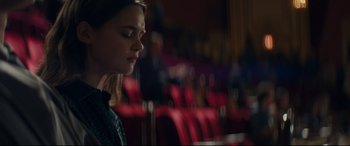 Movie still from “Cherry” (2021), directed by Joe Russo – A woman sitting in front of red chairs in an auditorium; Medium shot, Over the shoulder angle