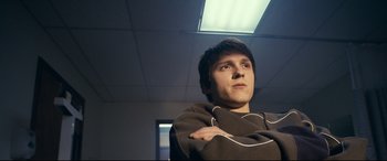 Movie still from “Cherry” (2021), directed by Joe Russo – A young man with his arms crossed in an office setting; Close Up shot, Low angle