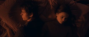 Movie still from “Cherry” (2021), directed by Joe Russo – Two children are laying in a bed together; Medium shot, Overhead angle