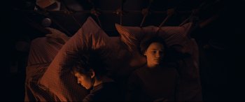 Movie still from “Cherry” (2021), directed by Joe Russo – A couple of people that are laying in a bed together; Medium shot, Overhead angle
