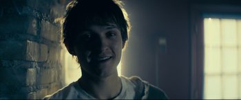 Movie still from “Cherry” (2021), directed by Joe Russo – A young man smiling for the camera in a dark room; Close Up shot, Low angle