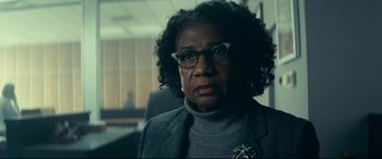 Movie still from “Cherry” (2021), directed by Joe Russo – An older woman wearing glasses and a gray jacket; Close Up shot, Over the shoulder angle