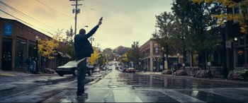 Movie still from “Cherry” (2021), directed by Joe Russo – A man holding a cell phone up in the rain; Wide shot, Low angle