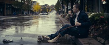 Movie still from “Cherry” (2021), directed by Joe Russo – A man sitting on the side of the road drinking coffee; Wide shot, Low angle