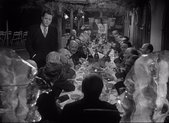 Movie still from “Citizen Kane” (1941), directed by Orson Welles – A black and white photo of people sitting at a dinner table; Medium shot, High angle