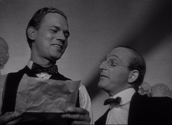 Movie still from “Citizen Kane” (1941), directed by Orson Welles – Two men are standing next to each other and one is holding a piece of paper; Medium shot, Low angle