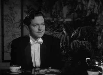 Movie still from “Citizen Kane” (1941), directed by Orson Welles – A black and white photo of a man sitting at a dinner table; Medium shot, High angle