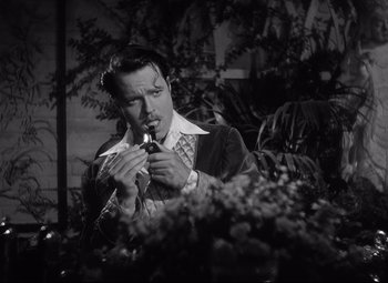 Movie still from “Citizen Kane” (1941), directed by Orson Welles – A black and white photo of a man holding a pipe; Close Up shot, Over the shoulder angle