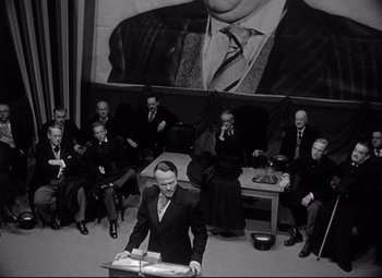 Movie still from “Citizen Kane” (1941), directed by Orson Welles – A man in a black suit is giving a speech to a group of people; Wide shot, High angle